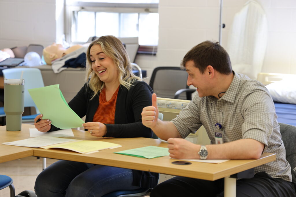 Male professor assisting female student at a desk.