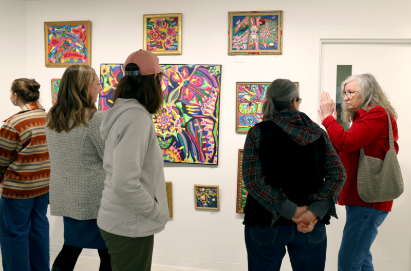 Five people in an art gallery looking at colorful abstract paintings.
